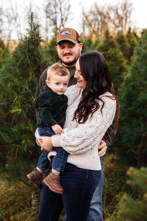 Family shares tender moment together among evergreen trees at Christmas tree farm.