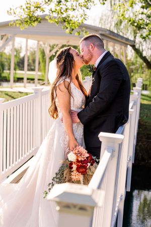 Newlyweds embrace on white bridge gazebo during sunset wedding photoshoot.