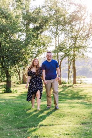 Couple walking and laughing together on a grassy hill during golden hour.