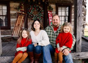 Family holiday portrait on rustic cabin porch with Christmas wreath and decorations.