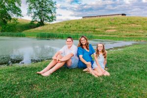 Family of three relaxing by a pond with rolling hills in the background.