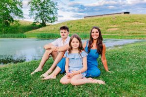 Family portrait by a pond with green hills and blue sky in the background.