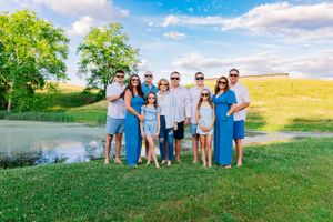 Group portrait of family members wearing blue and white outfits posed by a pond on sunny day.