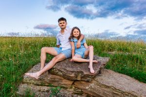 Couple sitting together on large rock formation against blue sky and rolling hills.
