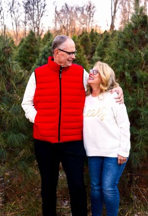 Couple in winter attire sharing tender moment among evergreen trees at sunset.