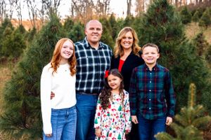 Smiling group poses for a festive holiday portrait surrounded by evergreen trees outdoors.