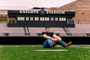 Man sitting on football field turf in front of Knights Stadium during golden hour.