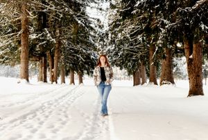 Someone walking through a snowy forest path lined with tall evergreen trees.