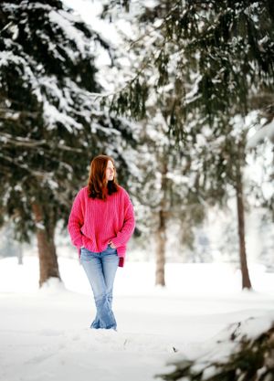 Figure in pink sweater and jeans walking through snowy forest path.