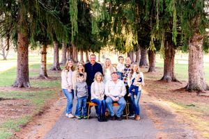 Large family group posed for portrait under evergreen trees on a pathway.
