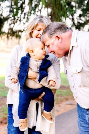 Three generations share an intimate moment together on a path surrounded by evergreen trees.