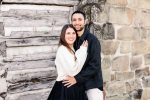 Couple in contrasting black and white sweaters embrace against rustic wall.