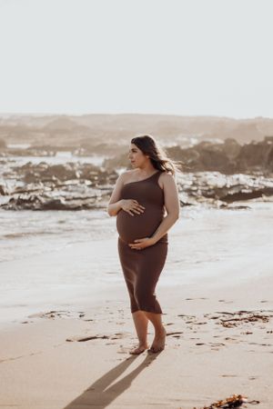 Pregnant woman holding her belly on the beach.