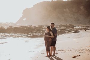 Pregnant woman and husband holding her belly on the beach.