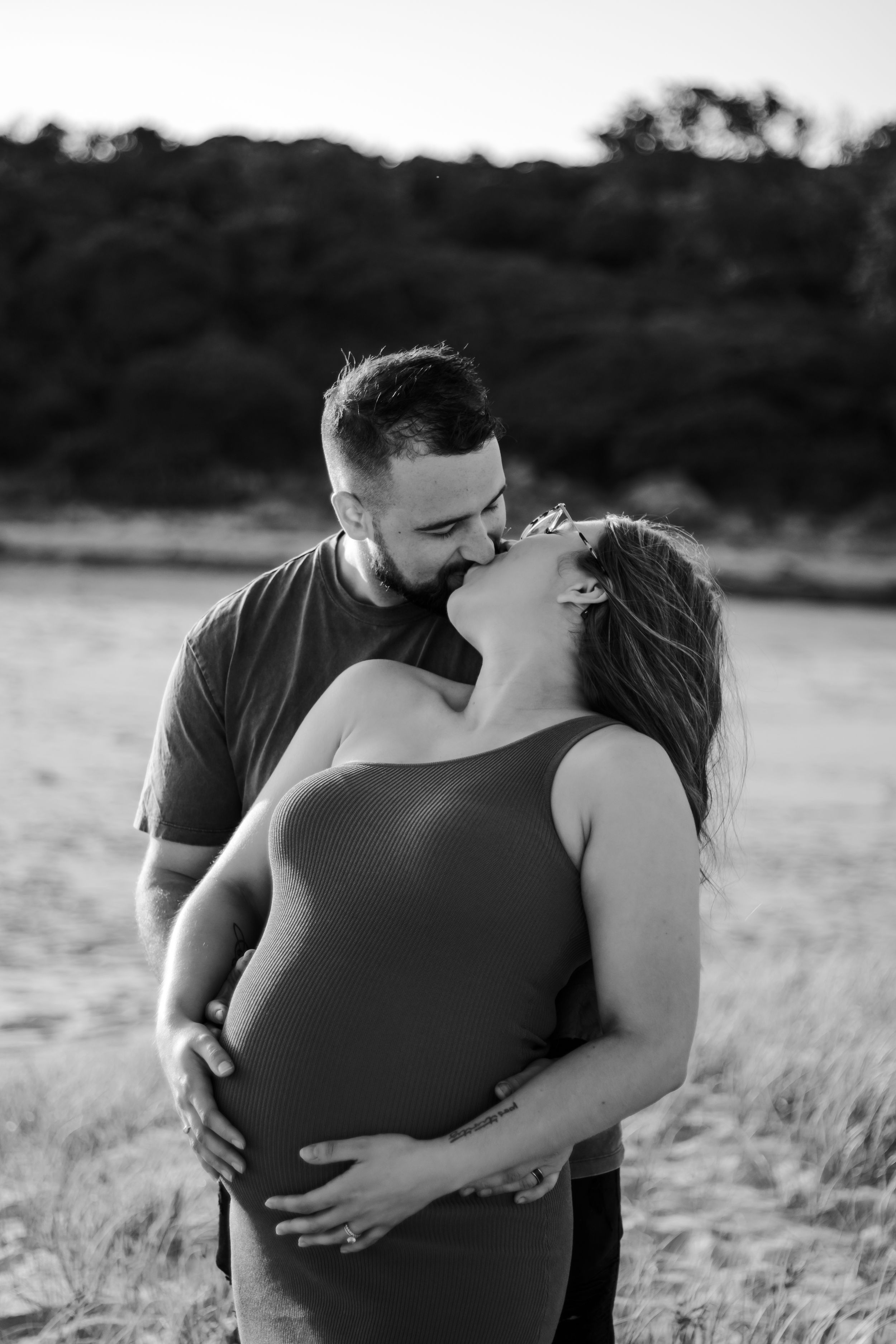 Pregnant woman and husband kissing and holding her belly on the beach.