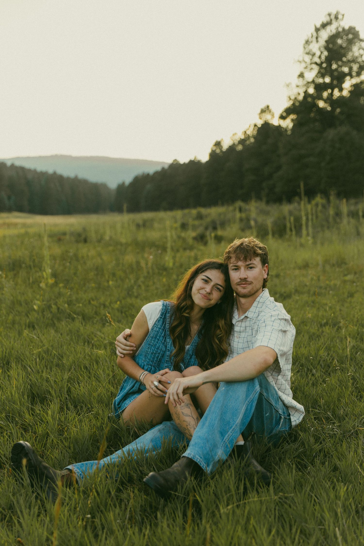 Couple relaxing together in a grassy meadow at sunset with mountains in the background.