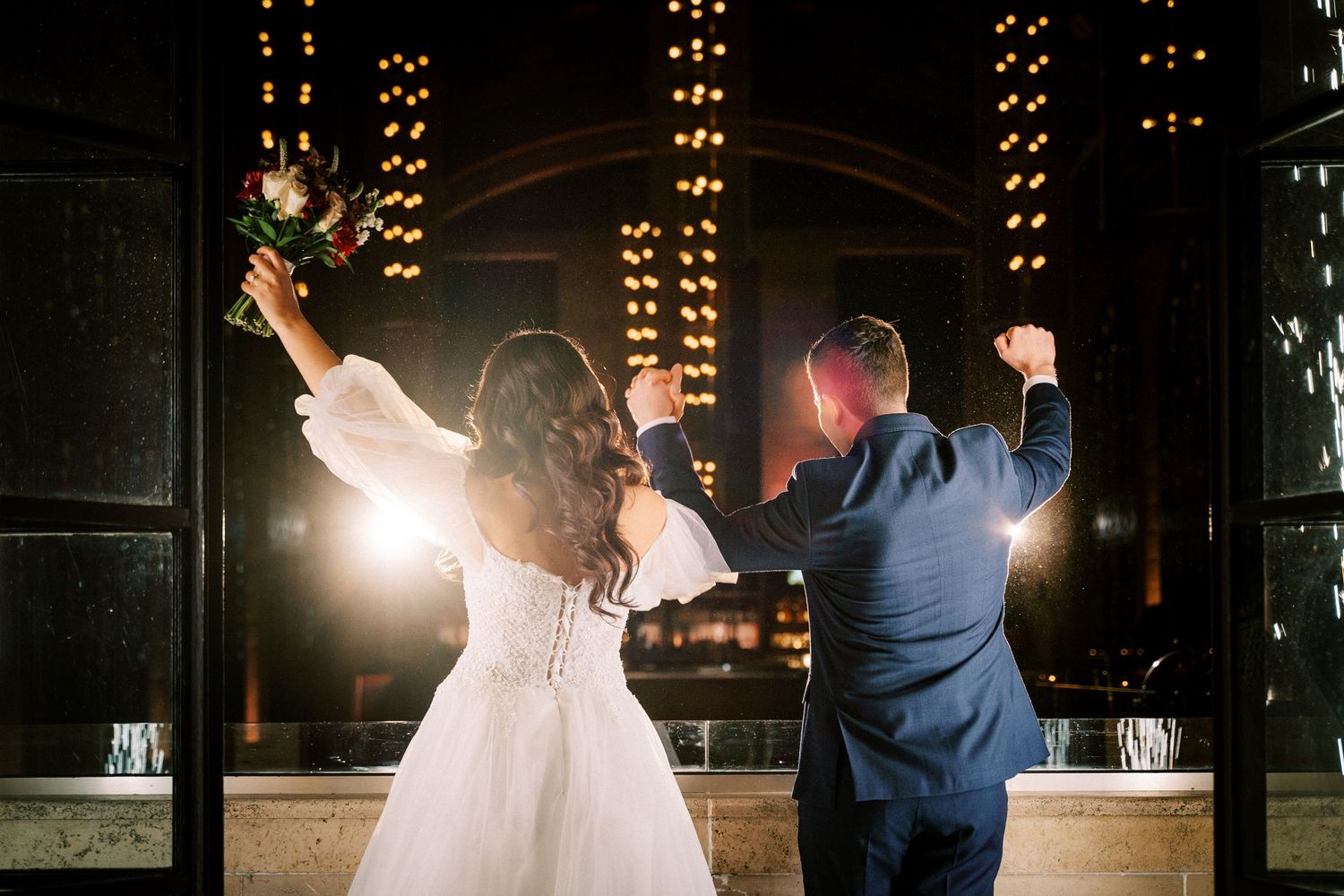 A couple celebrates on the dance floor during their wedding reception with dramatic backlighting.