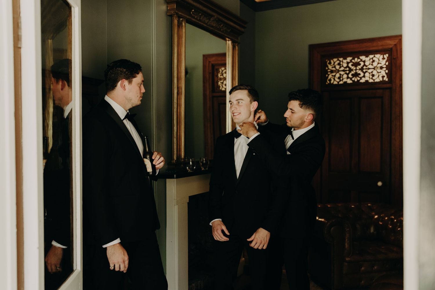 Groomsmen in black tuxedos gather in an elegant indoor venue for wedding photos.