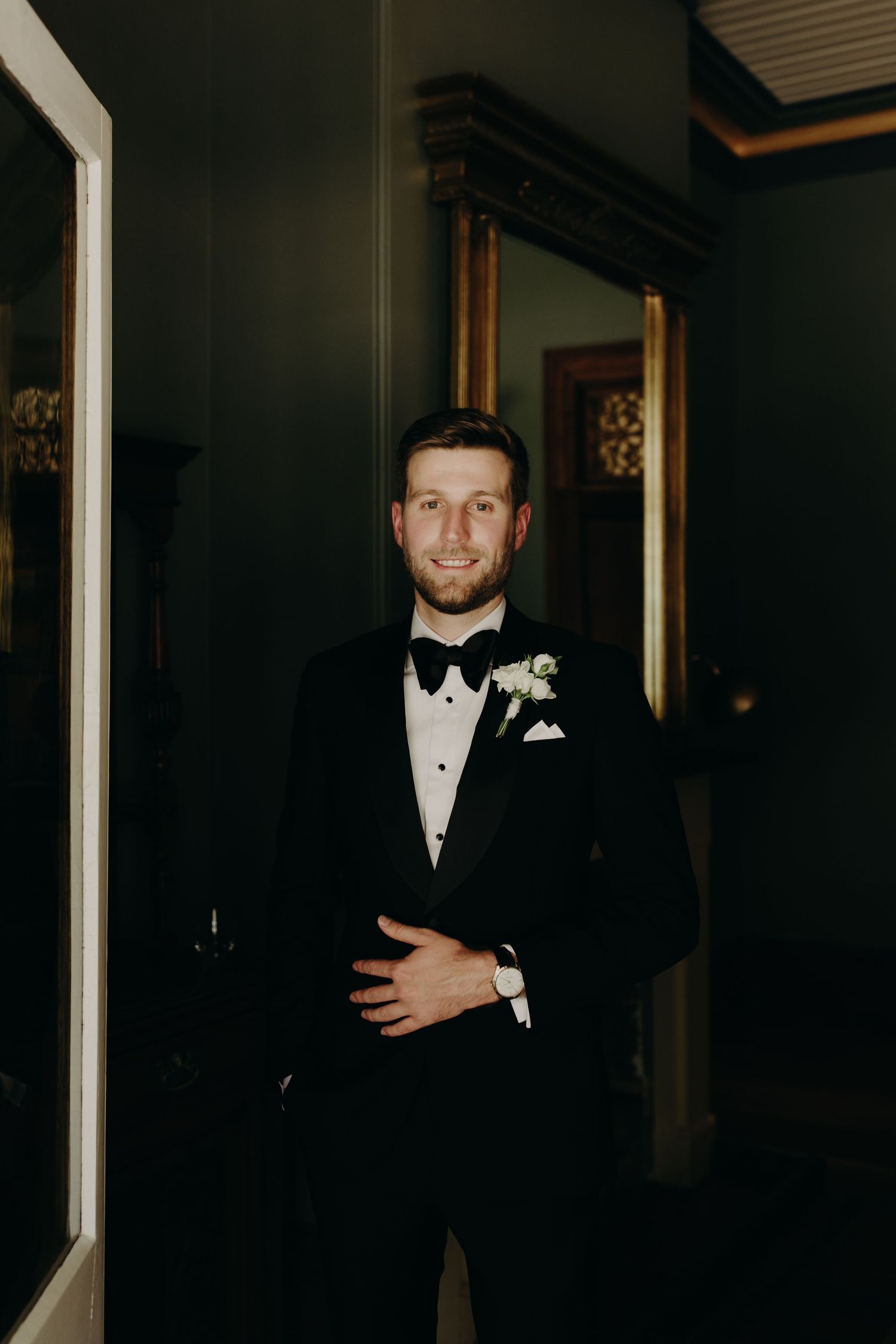 Groomsmen in formal black tuxedos and bow ties pose in a dimly lit room.