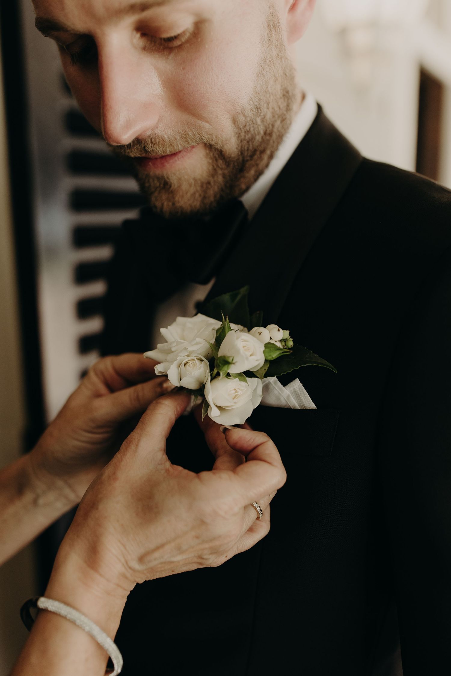 Close-up of white rose boutonniere being pinned on black tuxedo lapel.