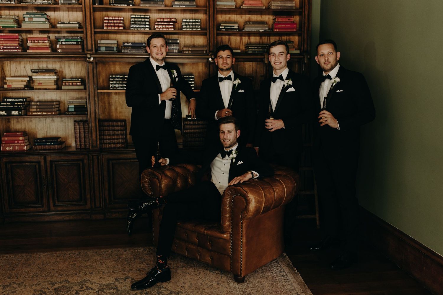 Wedding party relaxing in a library with leather furniture and bookshelves.