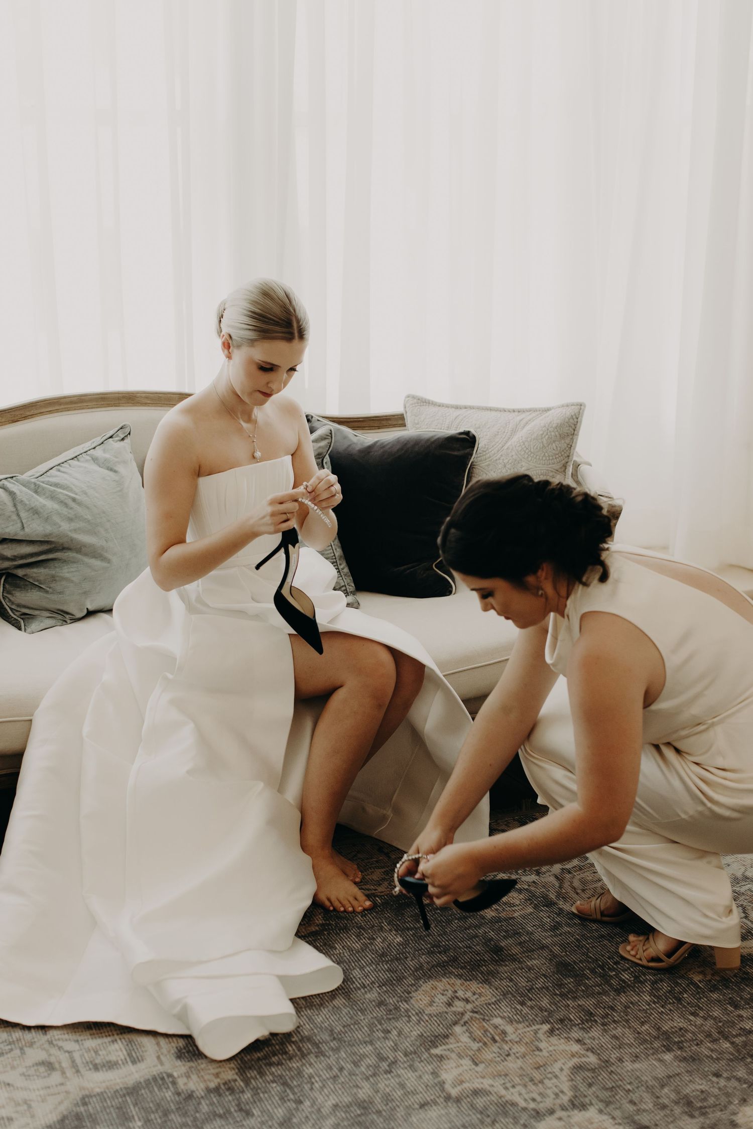 Wedding party helping with dress and shoe adjustments before ceremony.
