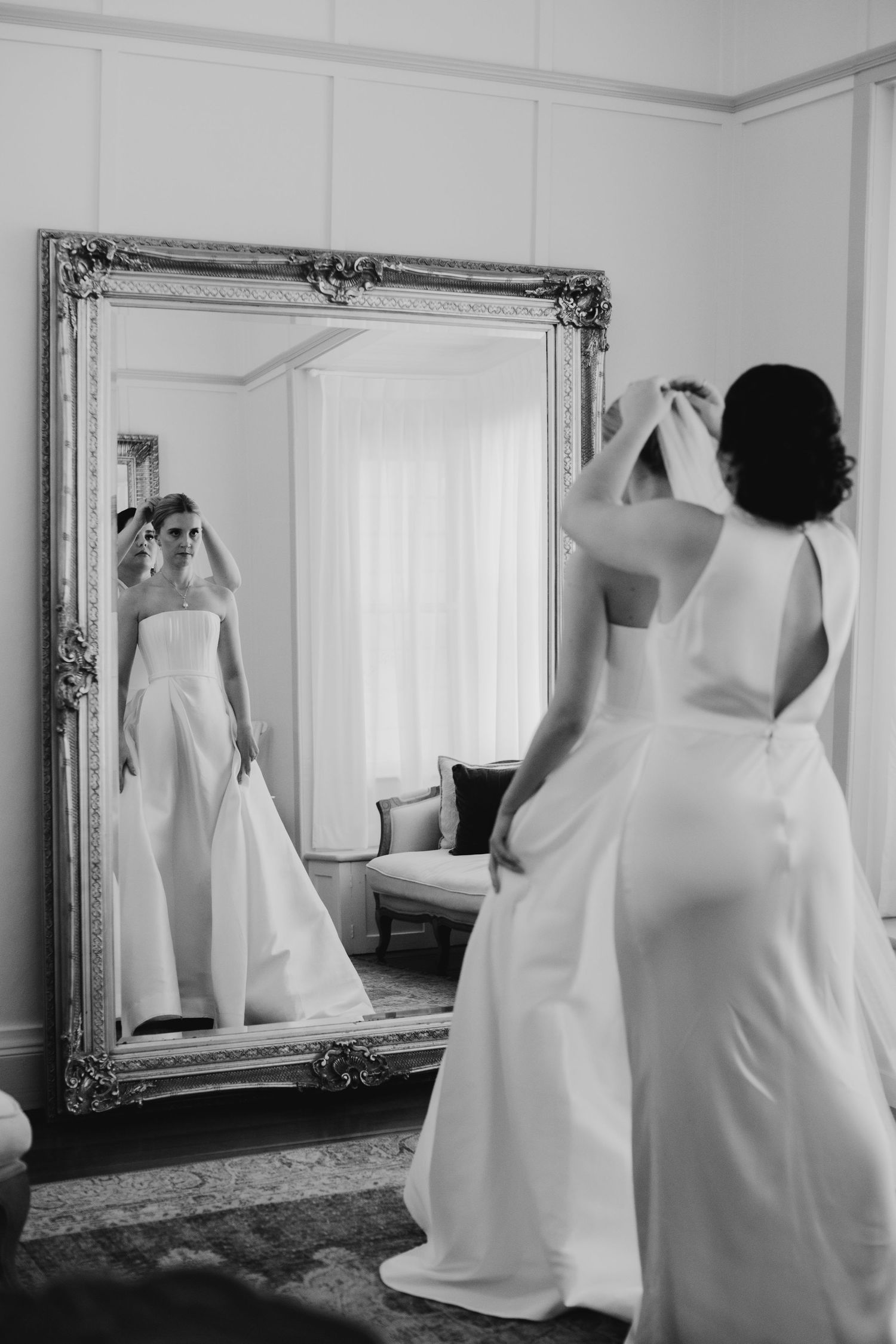 Black and white photo of wedding dress reflections in ornate framed mirrors.