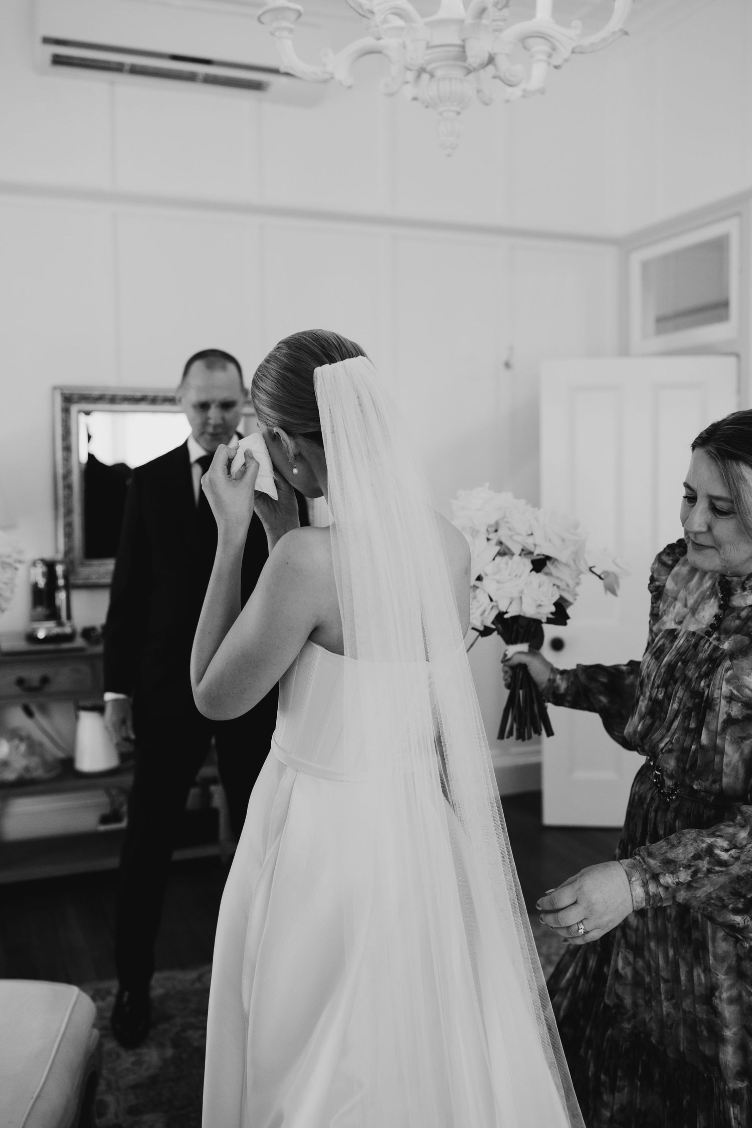 Black and white candid shots of wedding dress preparations with attendants helping.