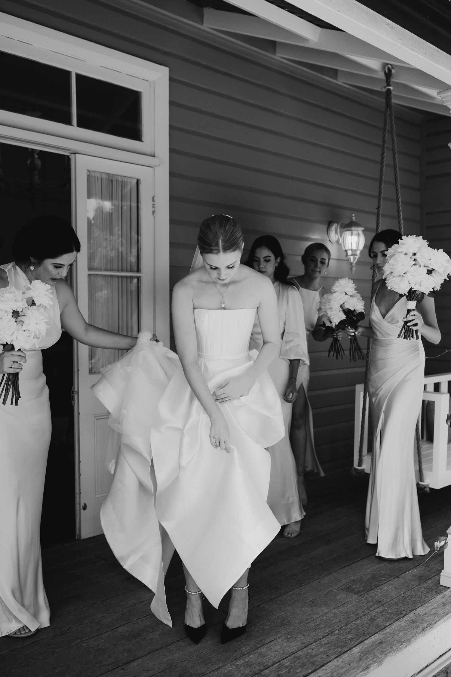 Wedding party lined up on porch wearing white dresses and holding bouquets.