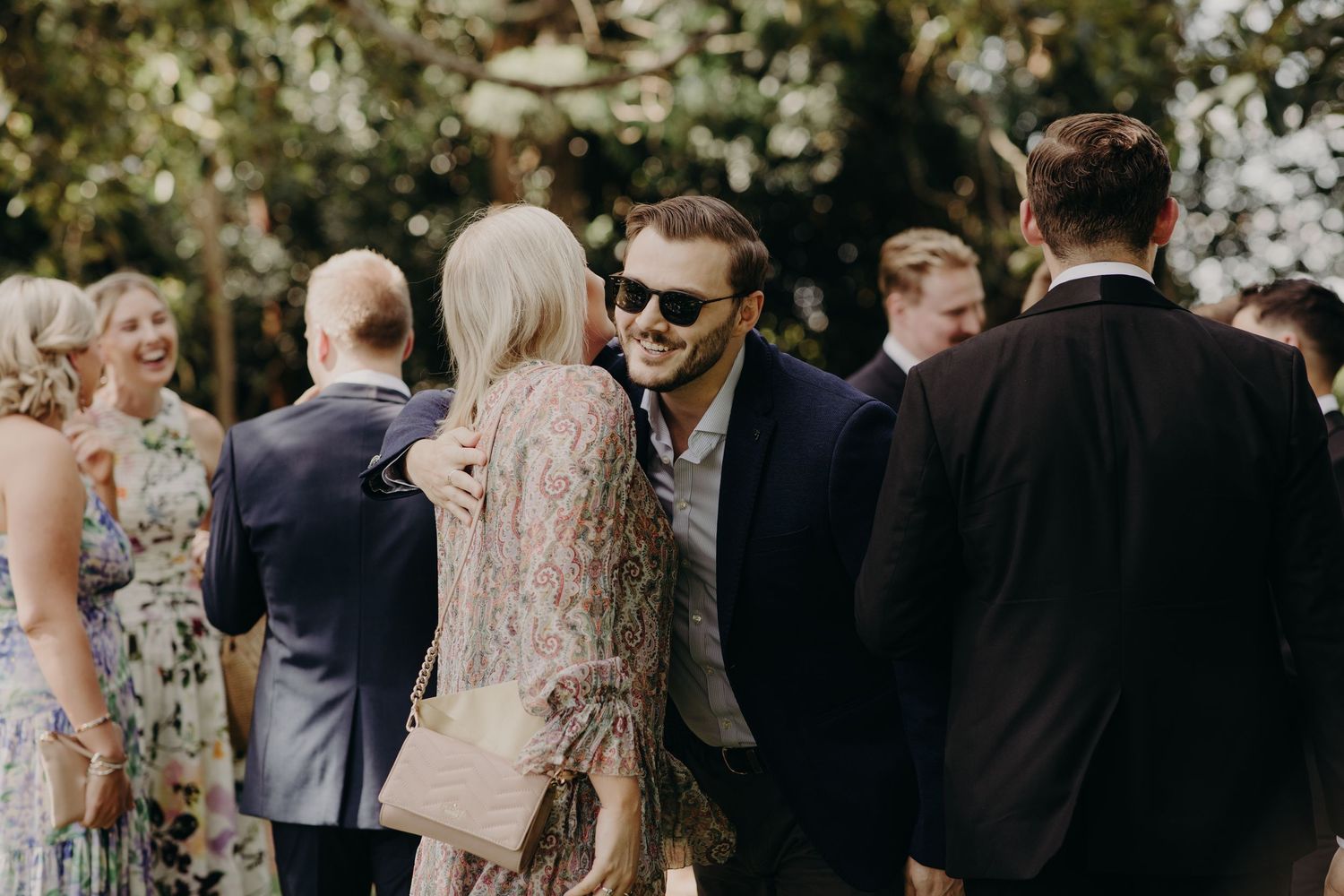 Wedding guests mingling outdoors in formal attire during daytime celebration.