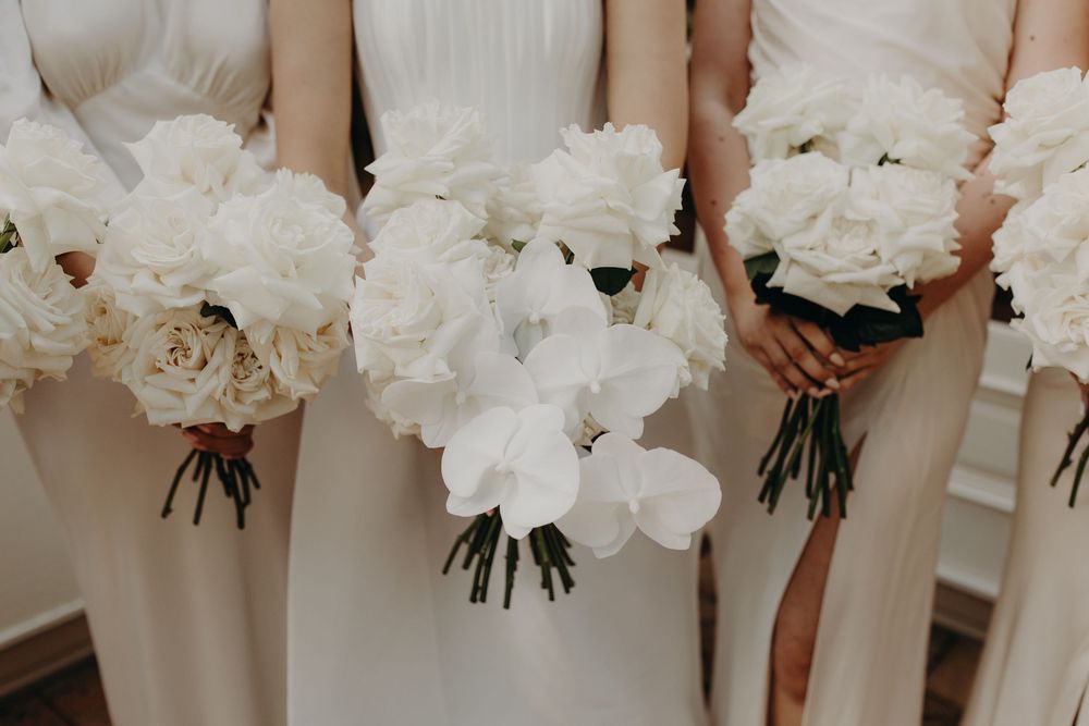 Close-up of white peony bouquets held by bridesmaids in matching dresses.