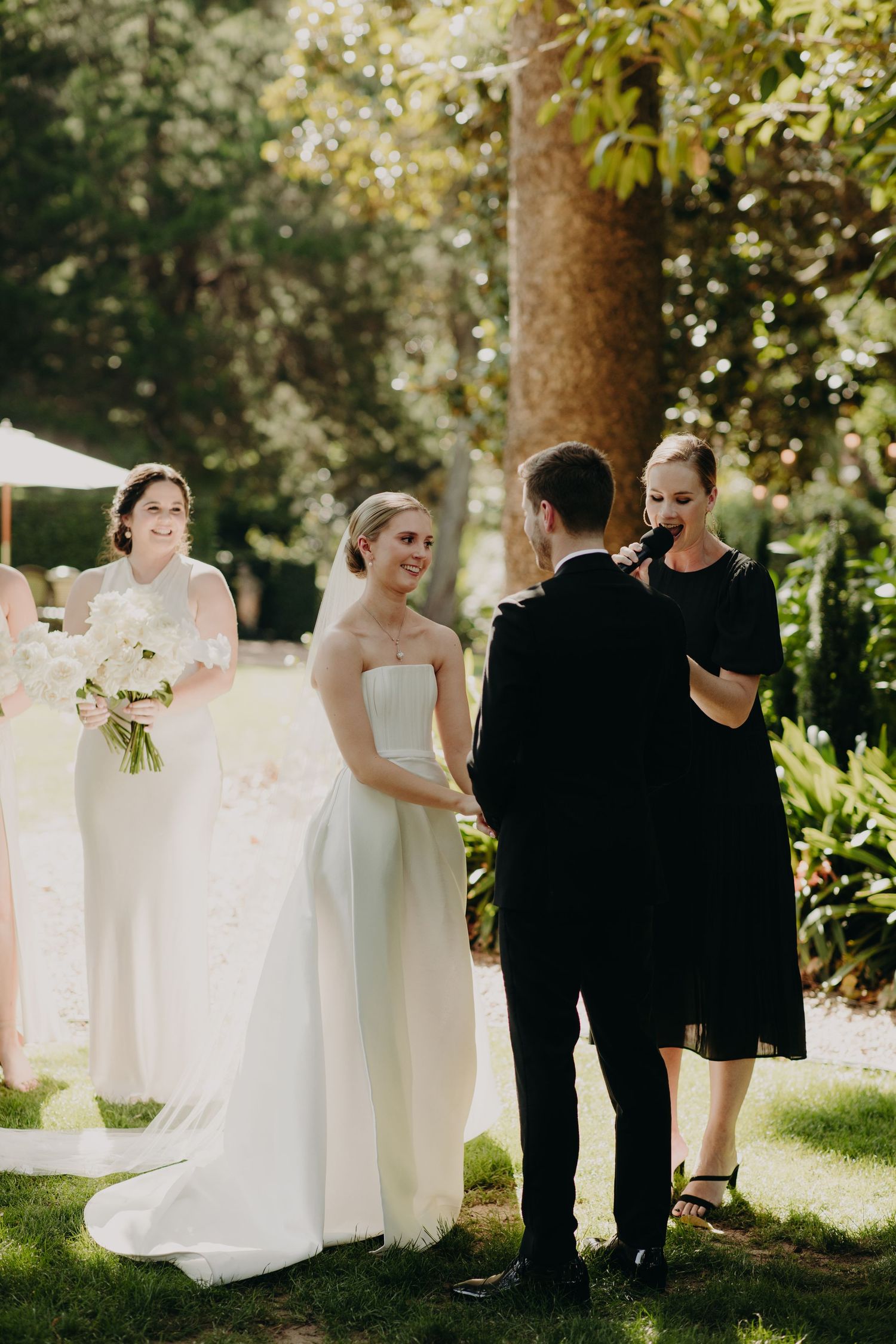 Wedding party poses for creative photos with white fabric in an outdoor garden setting.