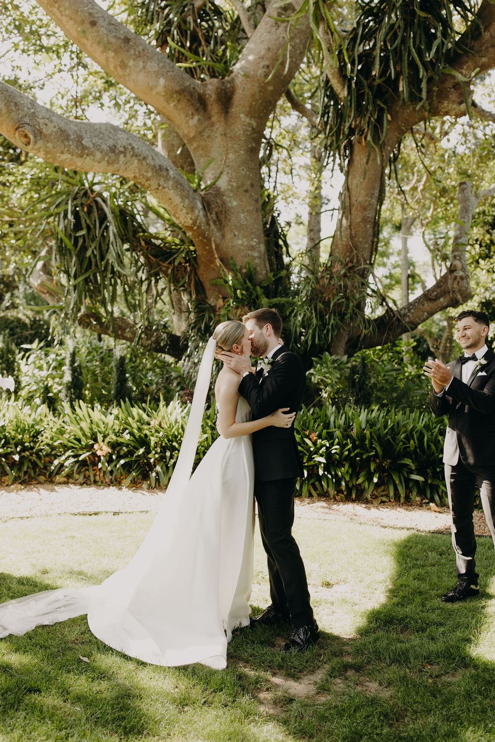 Wedding couple shares intimate moment under large tree during outdoor ceremony.