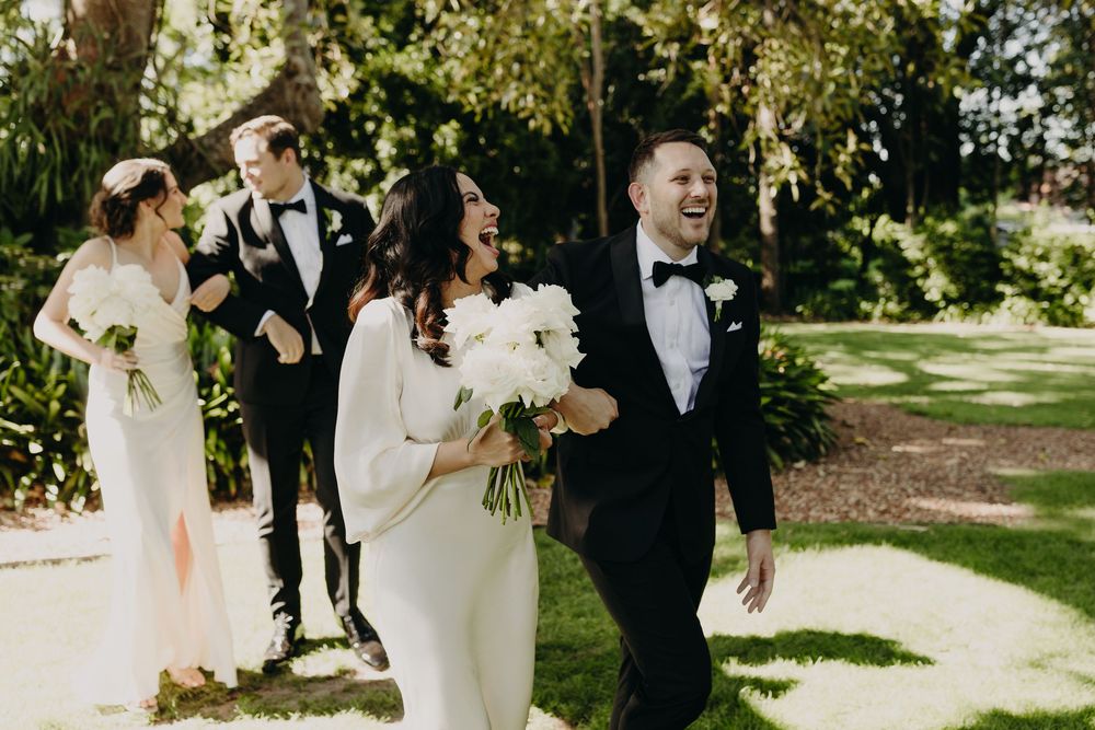 Wedding party poses together under trees during outdoor garden celebration.