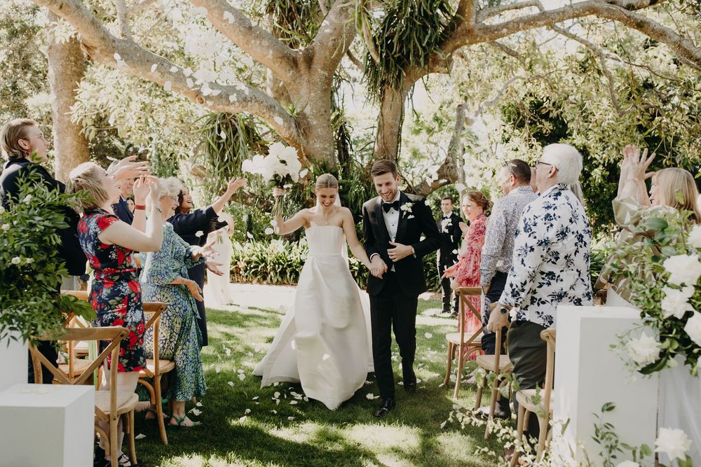 Outdoor garden wedding ceremony with floral decorations and seated guests.