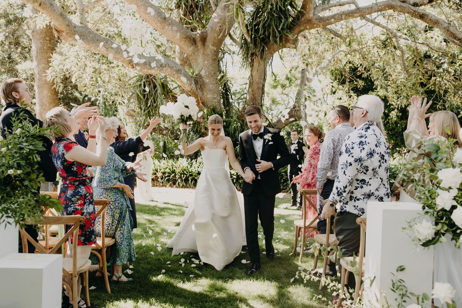 Outdoor garden wedding ceremony with floral decorations and seated guests.