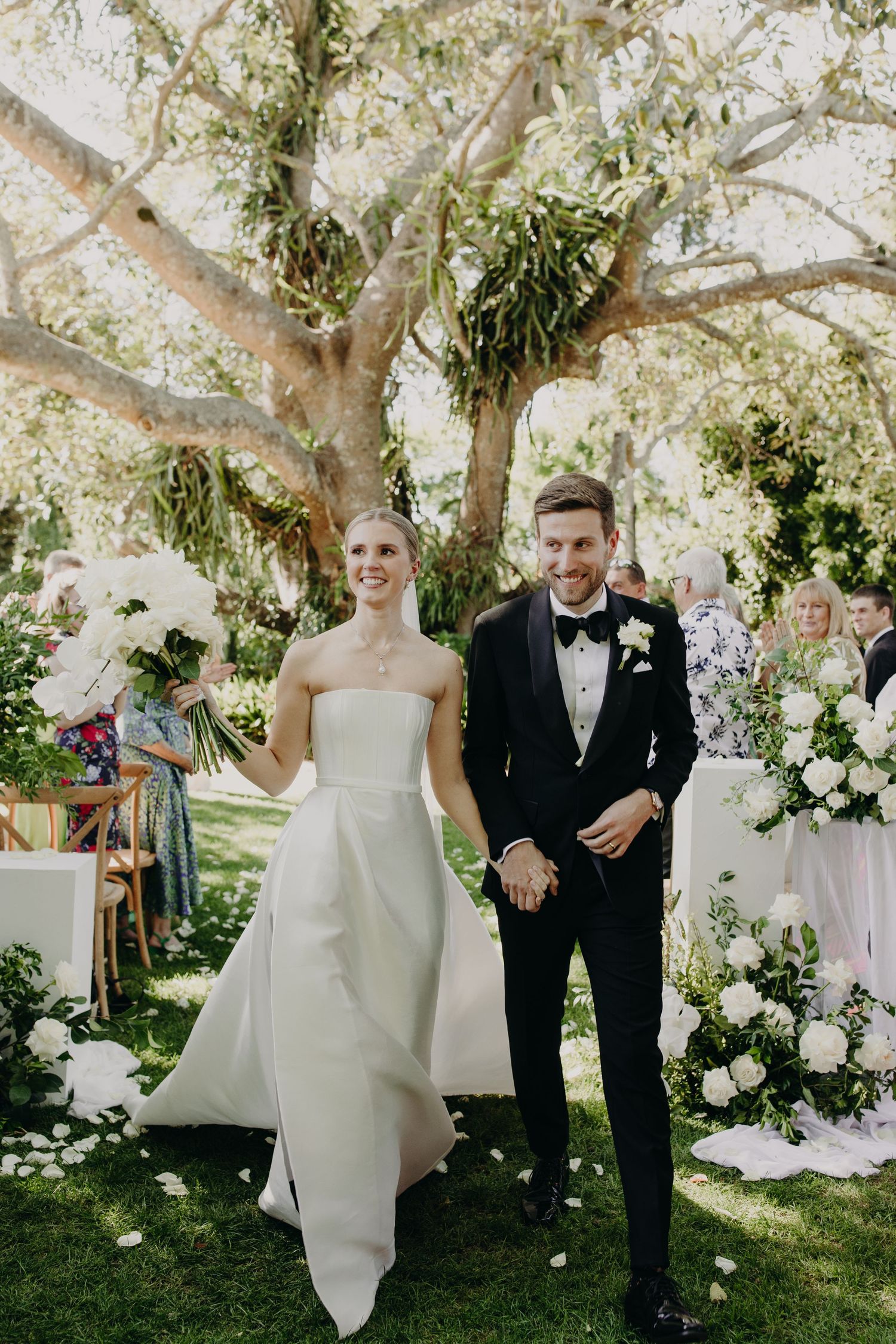 Elegant outdoor wedding ceremony under blooming trees with white floral arrangements.