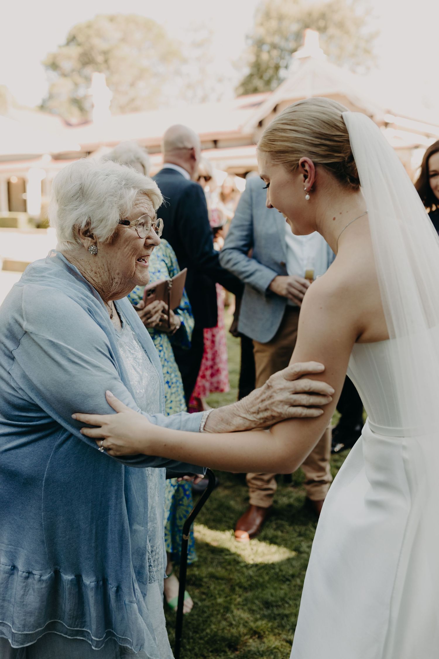 An emotional moment between a bride and elderly woman sharing embraces at an outdoor wedding celebration.