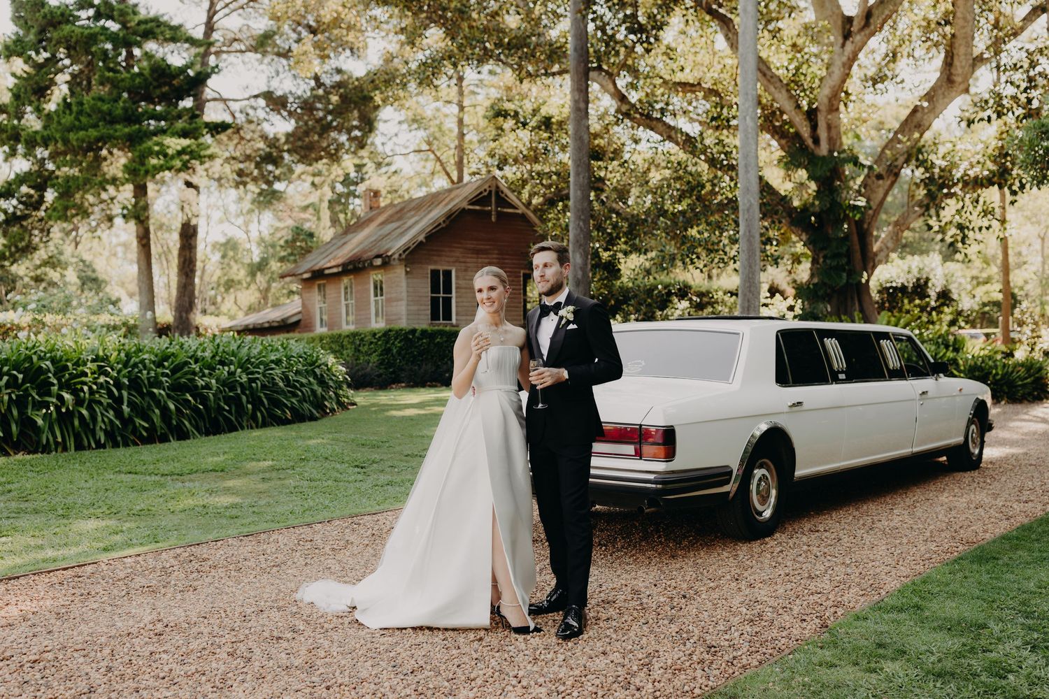 A classic white limousine parked on a tree-lined driveway during a wedding.
