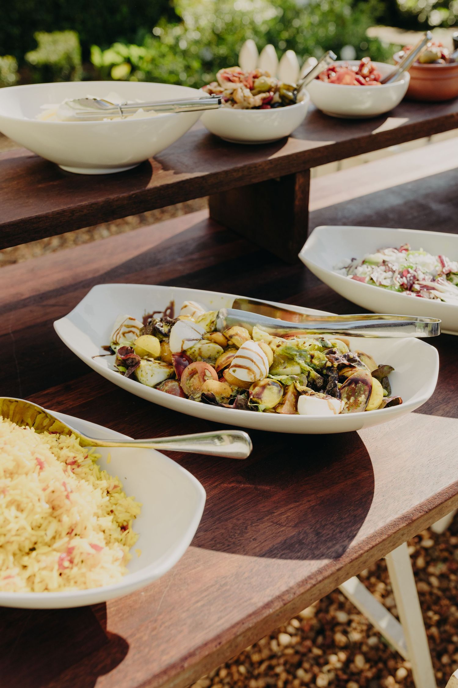 Elegant plated dishes arranged on a dark wooden table at an outdoor wedding reception.