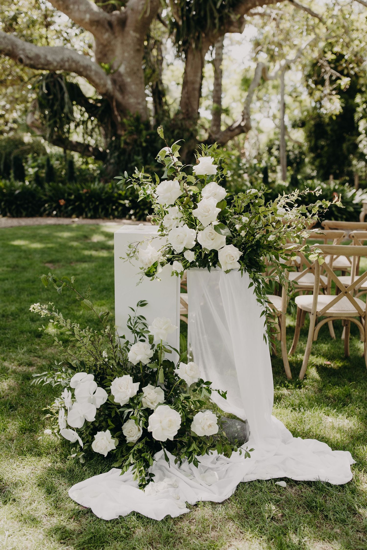 White floral arrangements with flowing fabric decorate a garden wedding ceremony space.