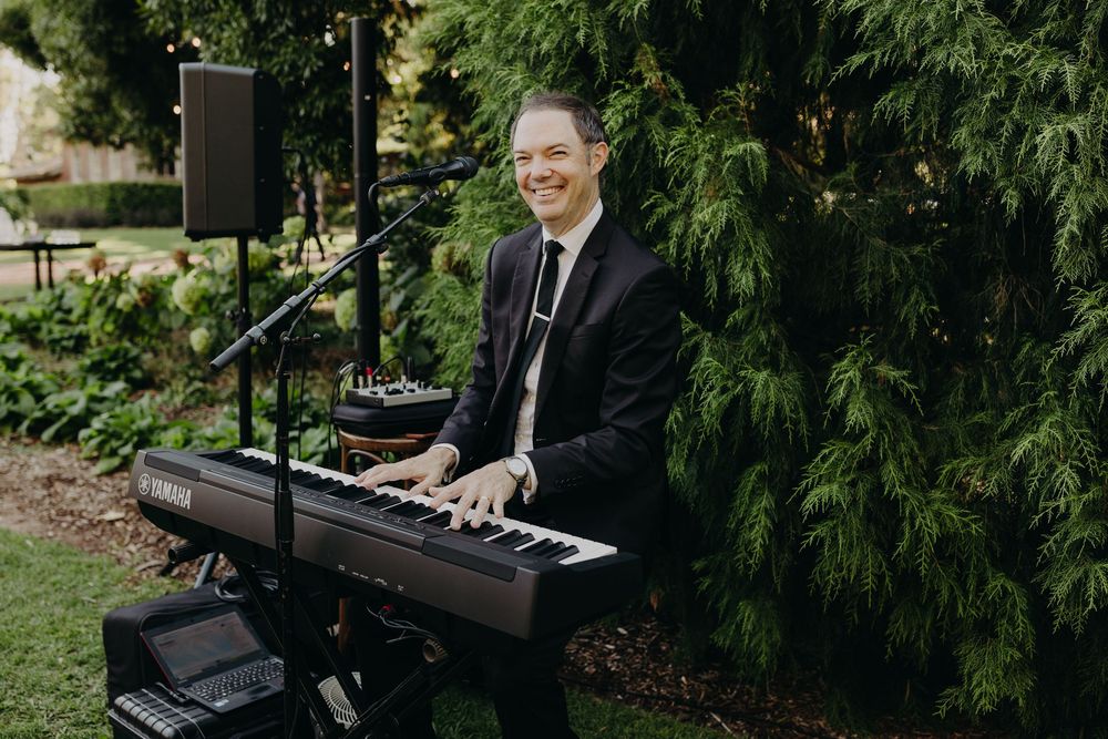 A pianist performs on a black piano during an outdoor garden event.