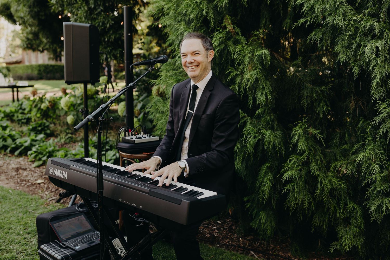 A pianist performs on a black piano during an outdoor garden event.