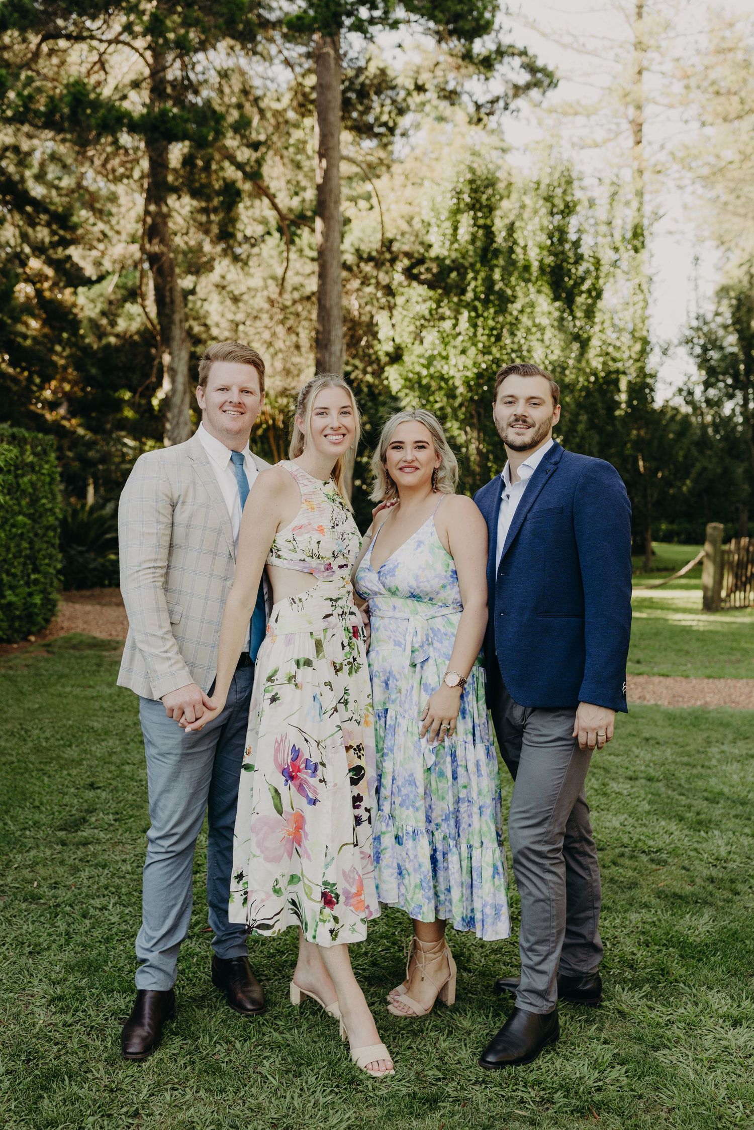 Wedding guests in floral spring dresses pose together on a sunny lawn.