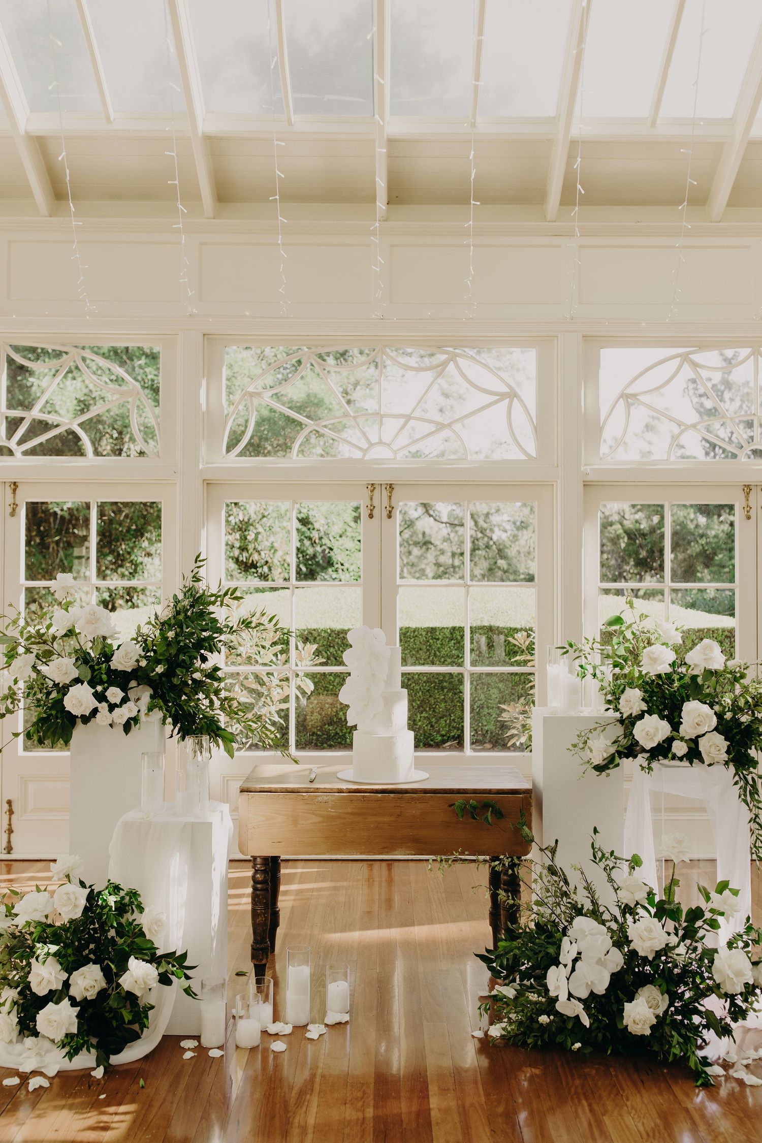 Sunlit conservatory decorated with white floral arrangements and greenery for an elegant wedding ceremony.