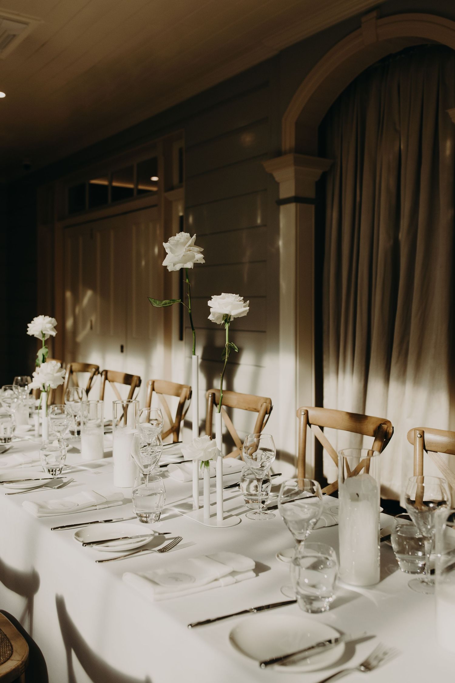 Formal dining tables set with white linens, tall candles and floral centerpieces in a dimly lit room.