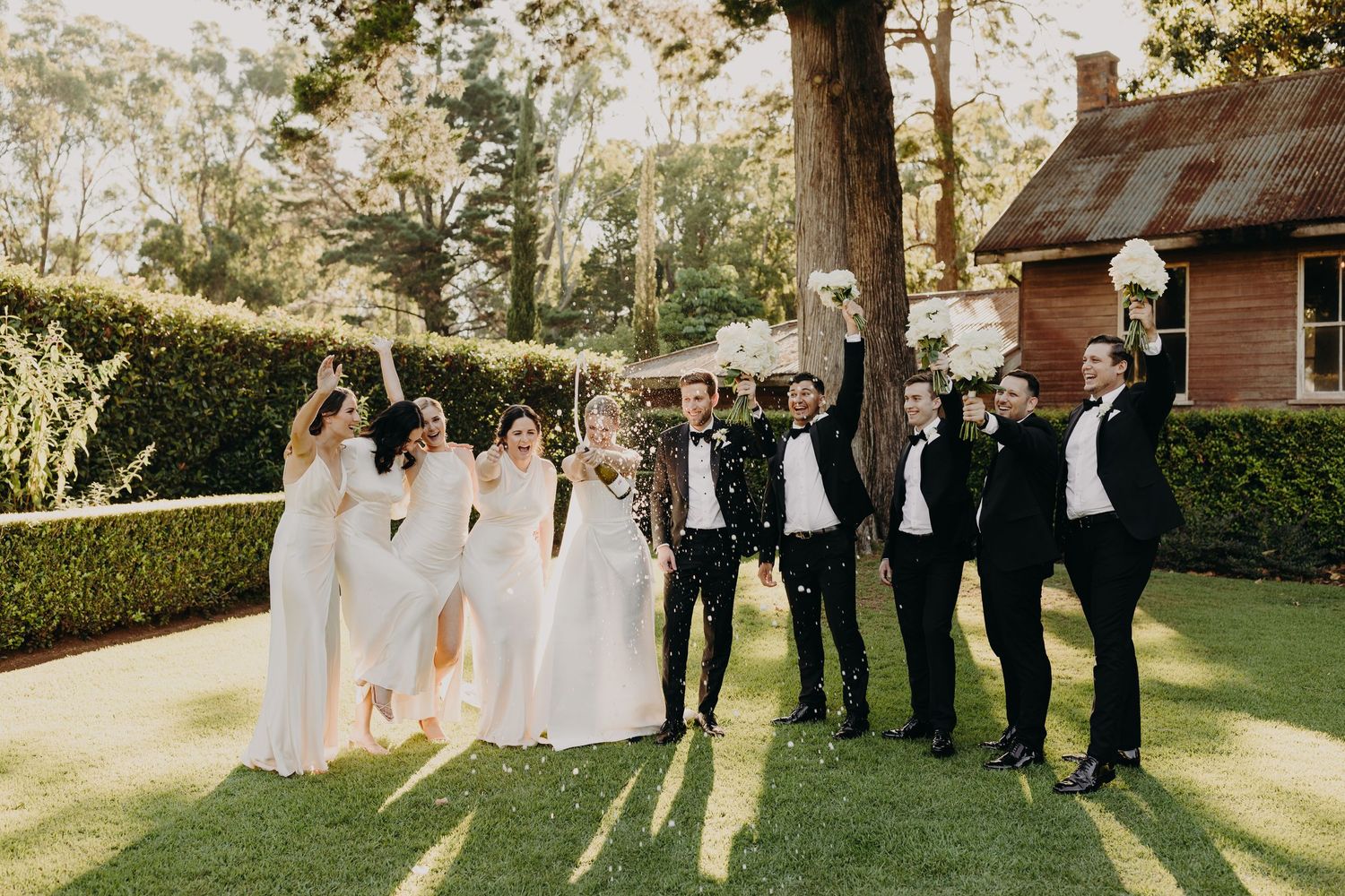 Candid wedding party photo with celebratory poses in late afternoon sunlight.