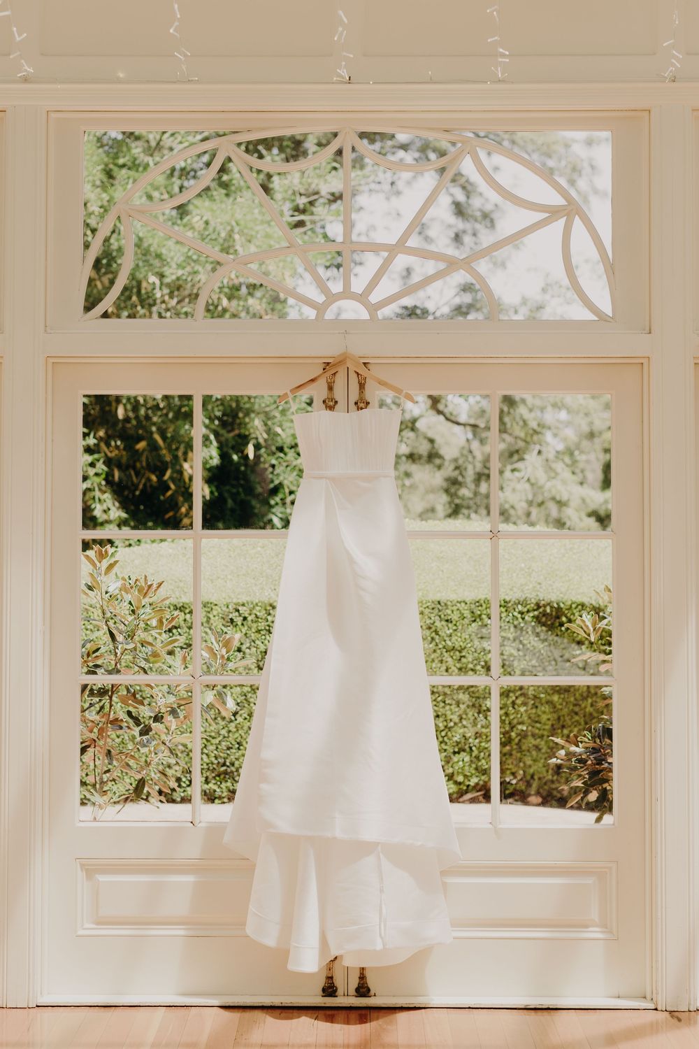 White wedding dresses hang elegantly in sunlit windows of a bridal preparation room.