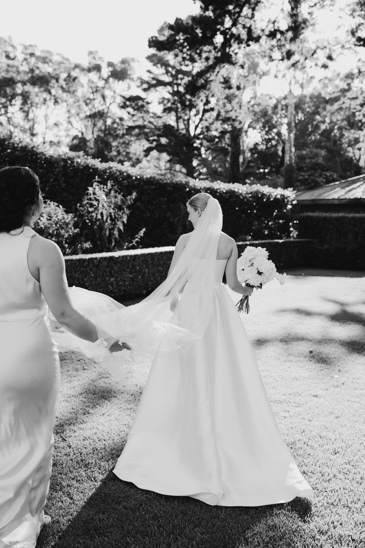 Elegant white wedding dress flows in breeze during outdoor black and white photo.
