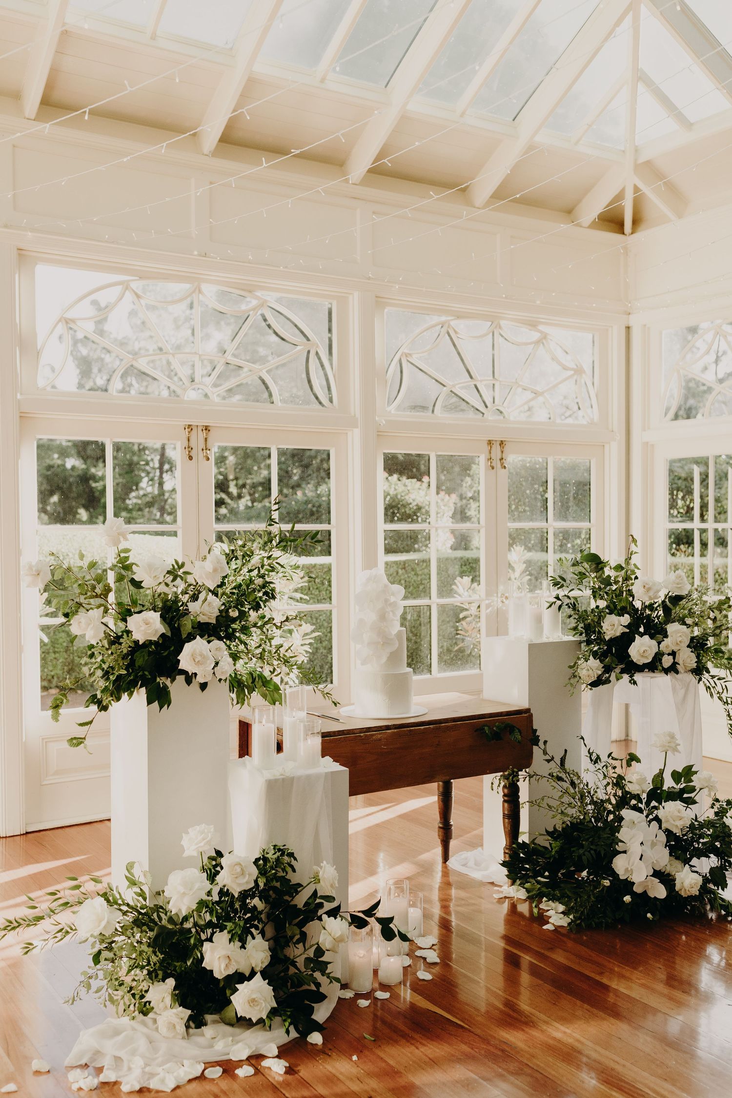 An elegant white conservatory wedding venue with hardwood floors and floral arrangements.